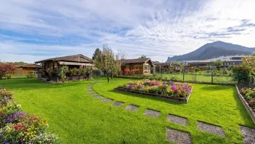 Weitläufiger Garten mit bunten Blumenbeeten, Steinpfad und Blick auf die umliegenden Berge.