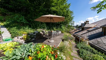 Sonniger Gartenbereich mit Holzterrasse, Sitzgelegenheiten und üppiger Bepflanzung, ideal zum Entspannen im Freien.