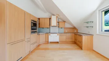 Helle Küche mit Holzschränken, Einbaugeräten und Dachschräge, bereit zur individuellen Gestaltung.