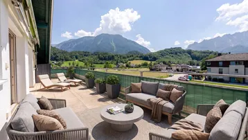 Große Sonnenterrasse mit bequemen Lounge-Möbeln und atemberaubendem Bergblick unter blauem Himmel.