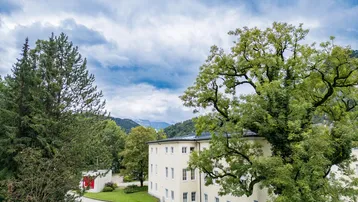 Historisches Gebäude umgeben von Bäumen mit Blick auf die umliegende Berglandschaft.