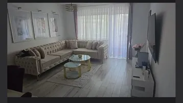 Helles Wohnzimmer mit großem Ecksofa, modernen Couchtischen und viel Tageslicht durch die Fenster.