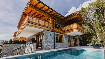 Moderne Chalet-Villa mit Stein- und Holzfassade, Balkonen und Infinity-Pool.