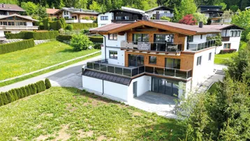 Modernes Chalet mit Holzfassade, mehreren Balkonen und einer Terrasse, umgeben von grüner Natur.