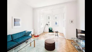 Helles Wohnzimmer mit Fischgrätparkett, einem blauen Sofa und einem Erker mit großen Fenstern.