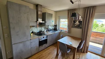 Moderne Küche mit grauen Schränken, Holzboden und Essbereich, direktem Zugang zum Balkon.