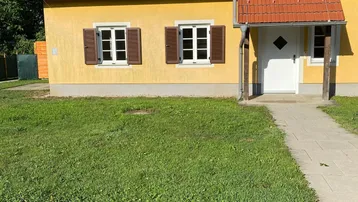 Gelbes Einfamilienhaus mit rotem Ziegeldach, braunen Fensterläden und grünem Vorgarten.