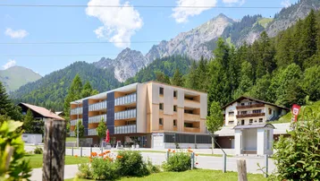 Modernes Gebäude mit Holzfassade und Balkonen, umgeben von grünen Bergen und Bäumen.