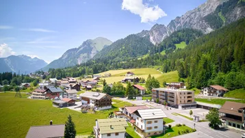 Weitläufige Ansicht eines Bergdorfes mit vielen Häusern und grünen Wiesen in einem Tal.