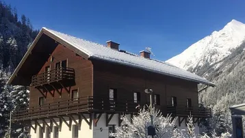 Traditionelles Holzhaus im alpinen Stil mit schneebedecktem Dach und Bergblick.