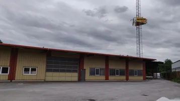 Gebäude mit gelber Fassade, roten Akzenten und großem Rolltor unter bewölktem Himmel.