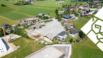 Luftaufnahme einer ländlichen Siedlung mit Wohnhäusern, grünen Feldern und einem See im Hintergrund.