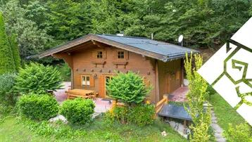 Charmantes Holzhaus im Chalet-Stil, umgeben von üppigem Grün und Bäumen.