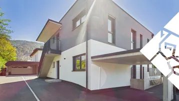 Modernes Mehrfamilienhaus mit klarer Architektur, Carport und sonniger Lage am Hang.