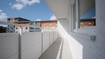 Langer, schmaler Balkon mit Sicherheitsnetz und Blick auf umliegende Wohngebäude unter blauem Himmel.