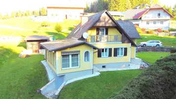 Gelbes Einfamilienhaus mit Satteldach und umliegendem Garten in ländlicher Umgebung.