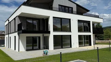 Modernes Mehrfamilienhaus mit weißer Fassade, großen Fenstern und Balkonen unter blauem Himmel.