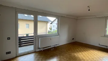 Helles Wohnzimmer mit Fischgrätparkettboden, großen Fenstern und Zugang zu einem Außenbereich.