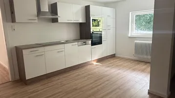 Moderne Einbauküche mit weißen Schränken, Holzarbeitsplatte und integrierten Geräten in einem hellen Raum.