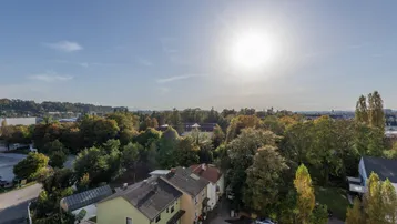 Weitläufiger Blick über die Stadt und grüne Baumlandschaften unter blauem Himmel.