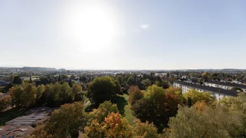 Weitläufiger Blick über die Stadt und grüne Parkanlagen unter strahlendem Sonnenschein.