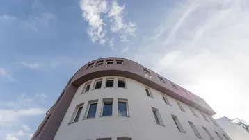Moderne Gebäudefassade mit geschwungenen Linien und zahlreichen Fenstern unter blauem Himmel.