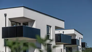 Moderne Wohnanlage mit weißer Fassade und schwarzen Balkonen unter klarem blauem Himmel.
