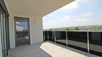 Geräumiger Balkon mit Fliesenboden, Glasgeländer und weitem Blick in die Landschaft.