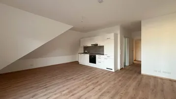 Heller Wohnbereich mit integrierter Küchenzeile, Laminatboden und Dachschrägen in einem Neubau.