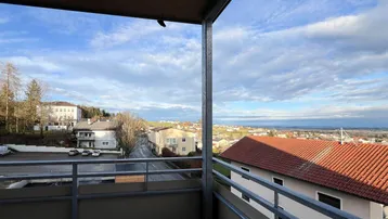 Balkon mit weitem Blick über die Dächer der Stadt und die umliegende Landschaft unter blauem Himmel.