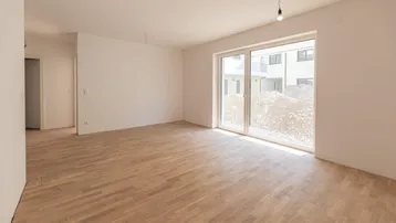 Helles, leeres Zimmer mit Parkettboden und Zugang zu einem Außenbereich, ideal für Wohn- oder Essbereich.