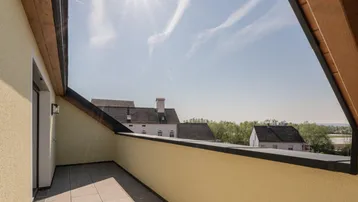 Sonnige Dachterrasse mit Fliesenboden und Blick auf die Umgebung unter blauem Himmel.