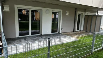 Gepflasterte Terrasse im Erdgeschoss mit Zugang zum kleinen Gartenbereich und großen Schiebetüren.