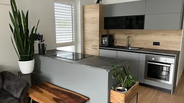 Moderne Küche mit grauen und holzfarbenen Schränken, einer Kochinsel mit Induktionskochfeld und einem Fenster.