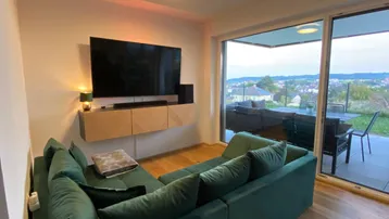 Modernes Wohnzimmer mit bequemer Couch, Holzboden und Zugang zur Terrasse mit Weitblick.