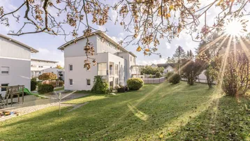 Sonnige Außenansicht des Gebäudes mit großem Rasenbereich, Spielplatz und Wäscheständer.