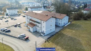 Luftaufnahme eines modernen Wohnkomplexes mit Parkplätzen und umliegenden Grünflächen.