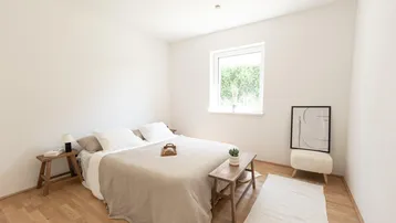 Ruhiges Schlafzimmer mit Holzboden, großem Fenster und Blick ins Grüne.