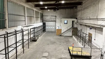 Geräumige Lagerhalle mit hohen Decken, Betonboden und Rolltor, bereit für die Renovierung.