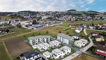 Luftaufnahme einer neuen Wohnsiedlung mit modernen Gebäuden, umgeben von grüner Landschaft und Feldern.
