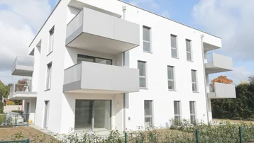 Modernes Mehrfamilienhaus mit weißer Fassade und mehreren Balkonen unter blauem Himmel.