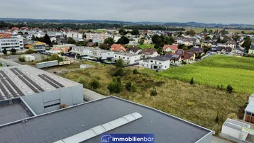 Luftaufnahme eines Mischgebiets mit Wohnhäusern, Gewerbebauten und landwirtschaftlichen Flächen unter bewölktem Himmel.