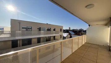 Heller Balkon mit Fliesenboden und Blick auf die umliegende Bebauung unter blauem Himmel.