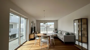 Helles Wohn- und Esszimmer mit Holzboden, großen Fenstern und Zugang zu einem Balkon.