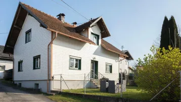 Ansicht des Einfamilienhauses von der Seite mit weißer Fassade und grünem Gartenbereich.