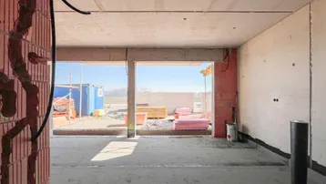 Rohbau eines hellen Wohnbereichs mit großen Öffnungen zur zukünftigen Terrasse.