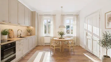 Helle, moderne Wohnküche mit beigefarbenen Schränken, Holzboden und Essbereich am Fenster.