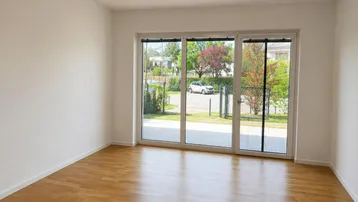 Helles, leeres Zimmer mit Parkettboden und großer Schiebetür zum Gartenbereich.