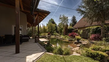 Überdachte Terrasse mit Sitzgelegenheiten und Blick auf den Teich und den gepflegten Garten.