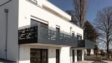 Moderne Wohnanlage mit weißer Fassade und stilvollen Balkonen unter blauem Himmel.